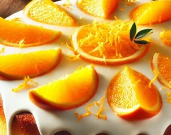 Um bolo de laranja cremoso, recém-assado, com cobertura brilhante e decorado com raspas e fatias de laranja.